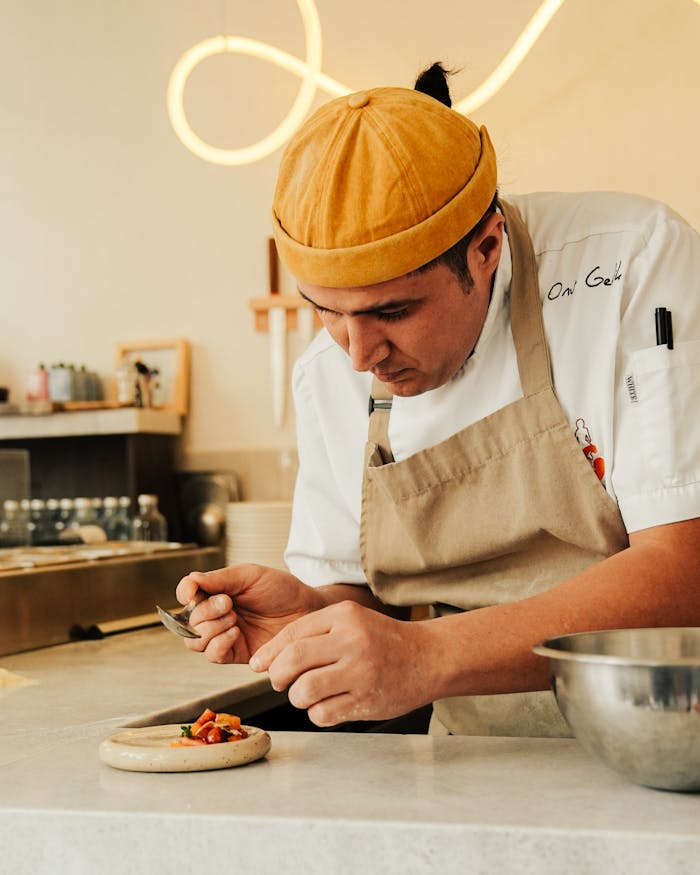 A chef intensely focuses on plating a dish in a stylish restaurant kitchen.