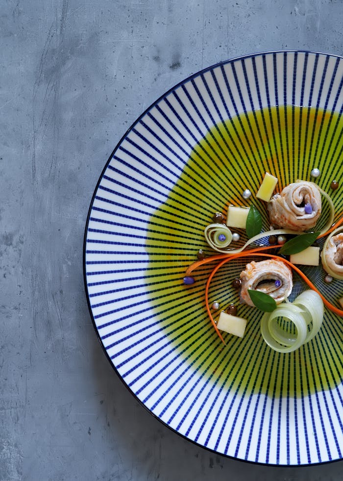 Elegant gourmet dish with fish and vegetables on a striped plate, top view.